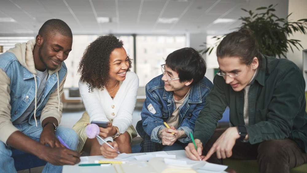 Four young adults smiling and looking at documents on a table